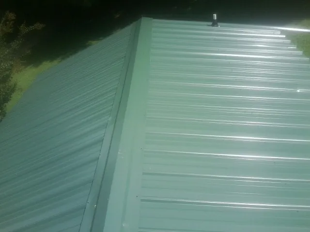 New green metal panels meeting at the ridge of a roof — Flat Roof Repair work by our crew in Taftville