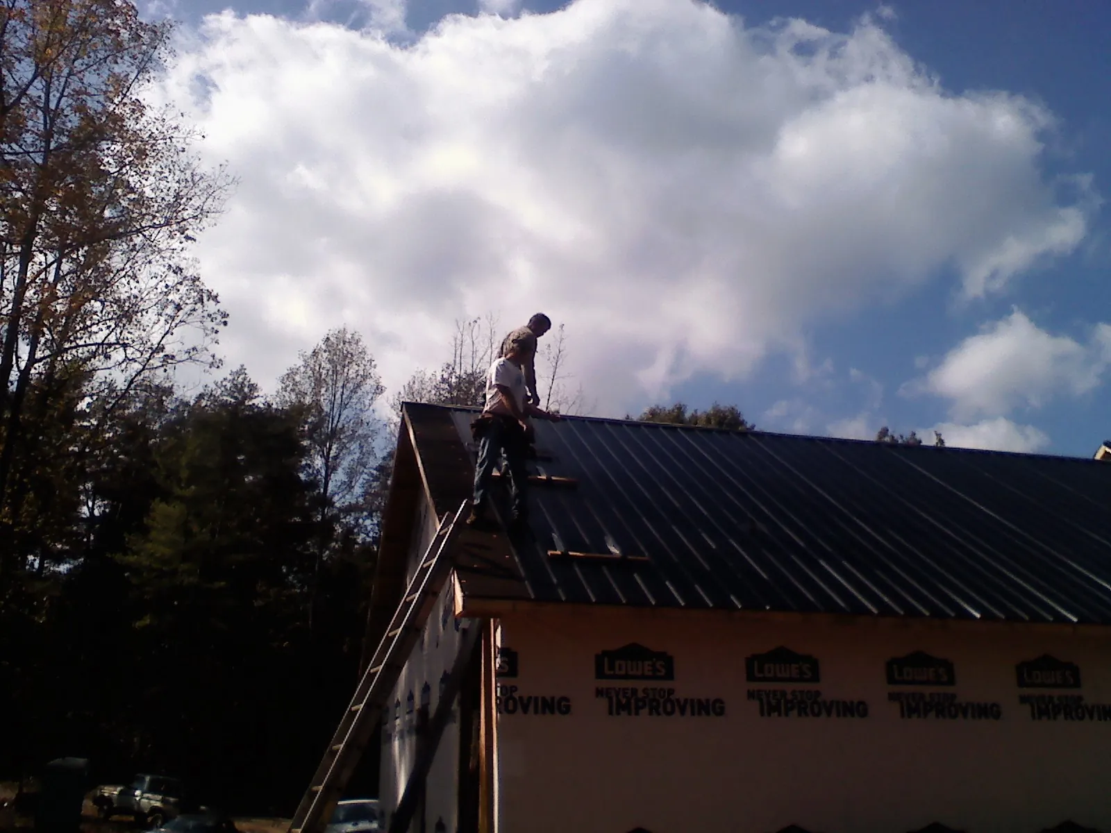 Roofer fastening dark metal panels high against a cloudy sky, from a Roof Inspection job in Taftville