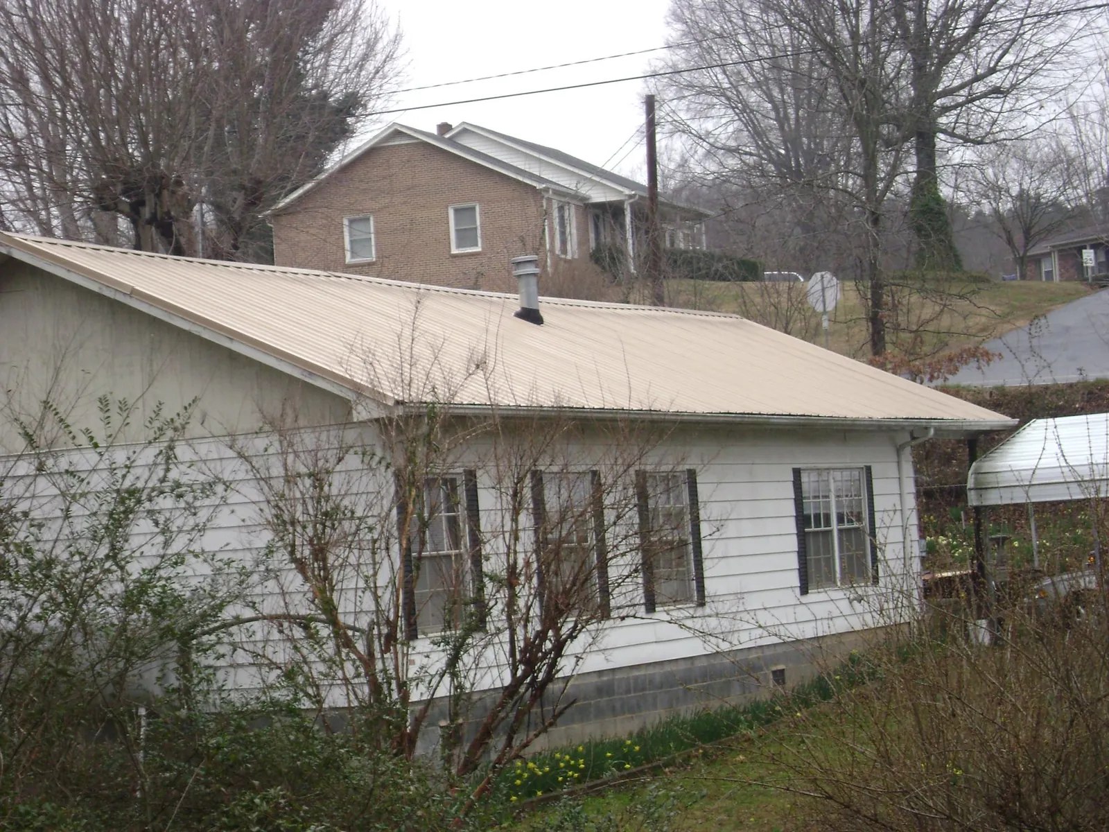 Tan metal roof on a white sided house set into a hillside — Commercial Roofing by Roofing Brothers in Taftville